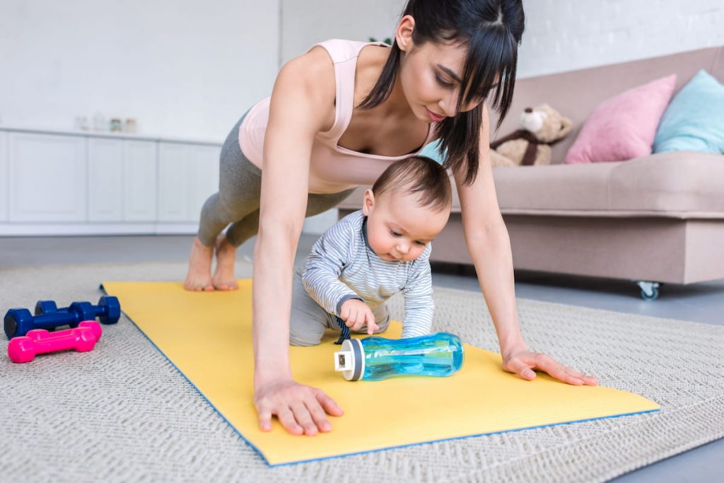 mother doing plank exercise on yoga mat with her child at home